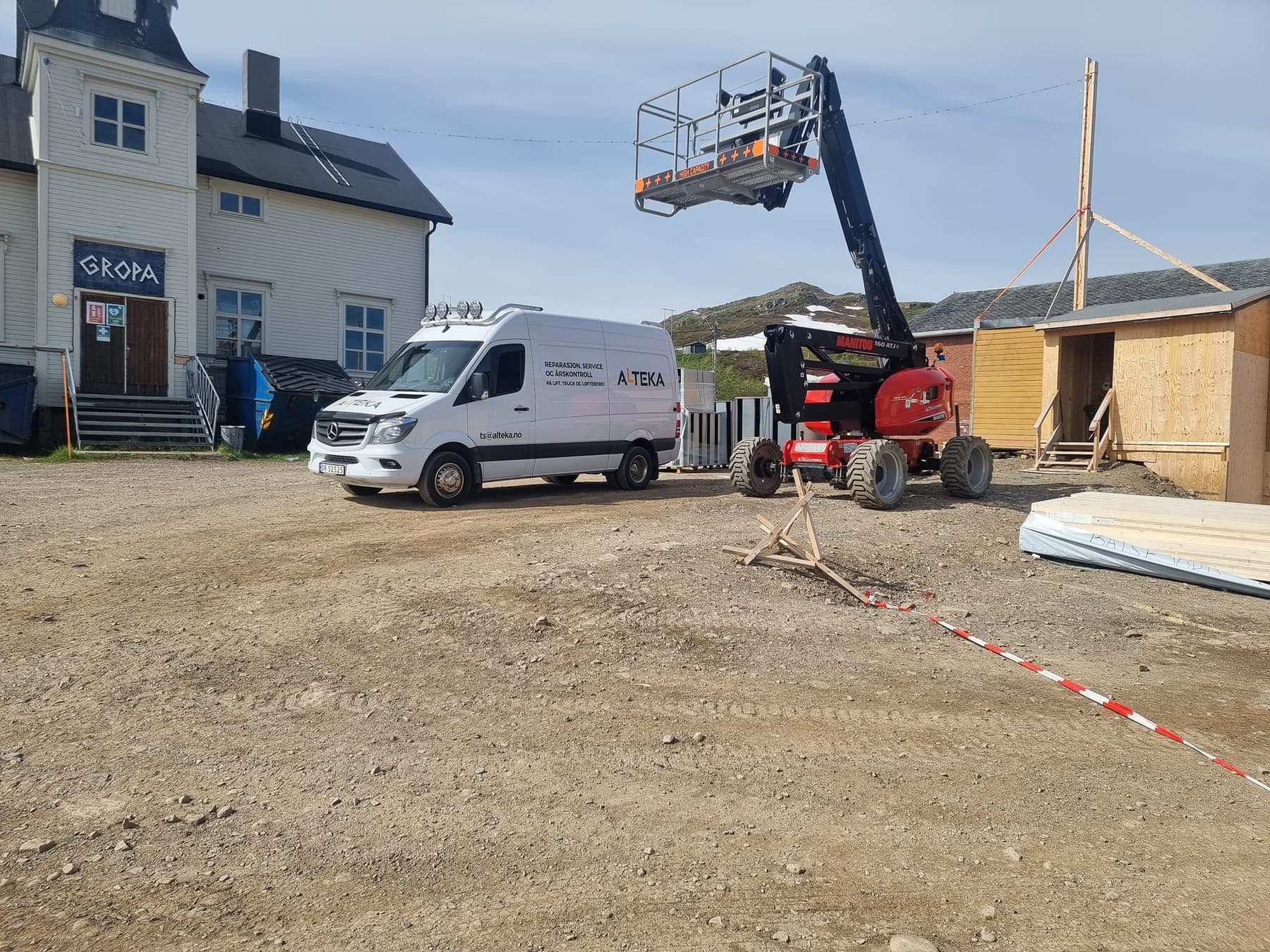 Servicebilen ved siden av en rød bomlift på en byggeplass ved sjøen